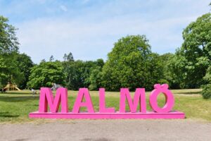 Malmöskylt i grön park som symboliserar Malmös olika bostadsområden